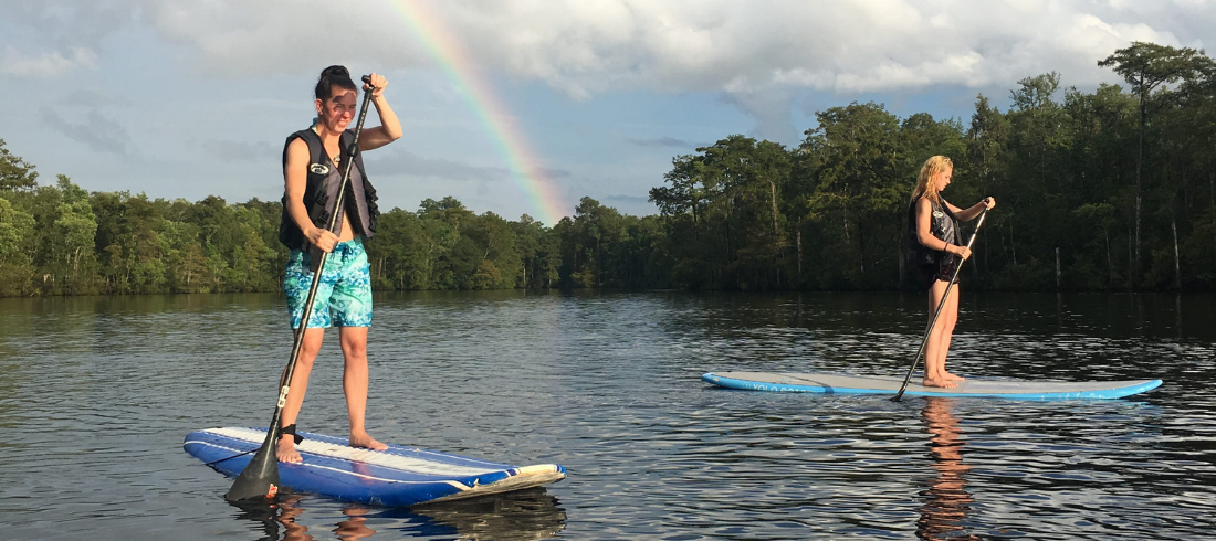 two people enjoying myrtle beach stand up paddleboarding in front of a rainbow